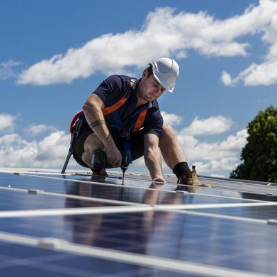 Ein Techniker mit einer Bohrmaschine bei der Installation von Photovoltaikanlagen auf dem Dach an einem sonnigen Tag.
