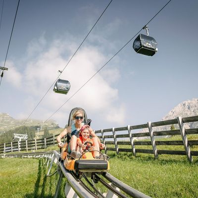 zwei Personen fahren mit der Sommerrodelbahn.