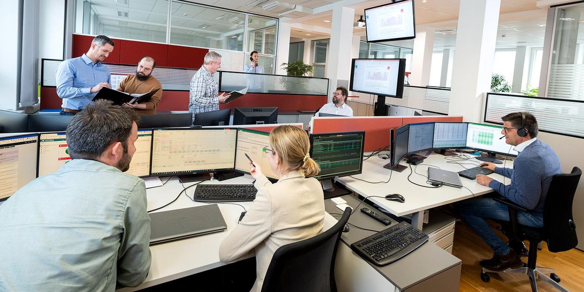 Mitarbeiterinnen und Mitarbeiter an ihre Schreibtische vor den Bildschirmen am Arbeiten und Besprechen.