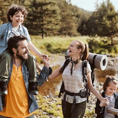 Eine Familie spaziert lachend durch Wiese und Wälder.