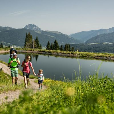 Eine Familie wandert neben einen kleinemSee entlang.