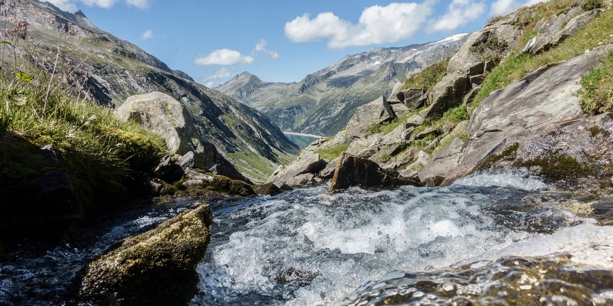 Wasser fließt zwischen den Steinen durch. Im Hintergrund sieht man Berge.