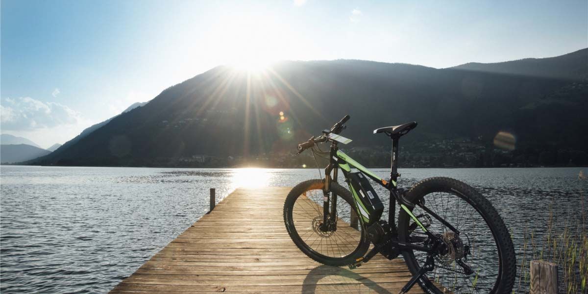 Rad steht an einem Steg. Run herum ist der See und die Sonne scheint hinter dem Berg heraus.