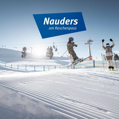 Skigebiet Nauders am Reschenpass: Ein junger Skifahrer hüpft über die Piste und ein Elternteil jubelt daneben.